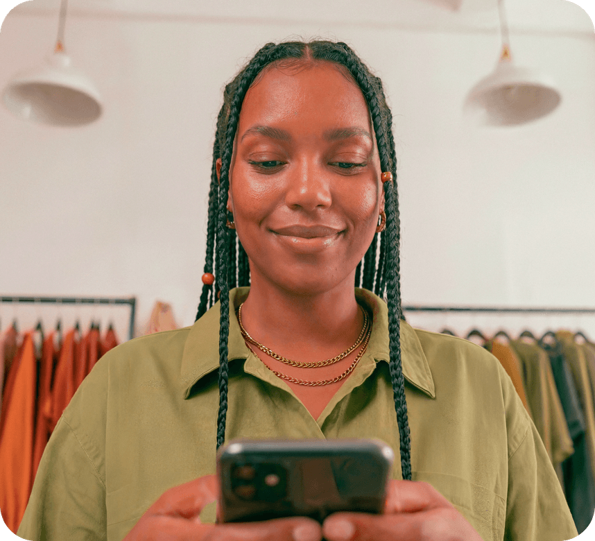 Empreendedora sorridente em sua loja de roupas consultando o celular