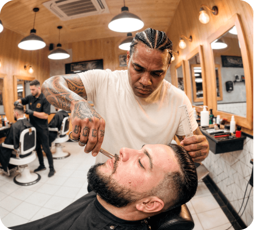 Barbeiro tatuado fazendo a barba de um cliente em barbearia