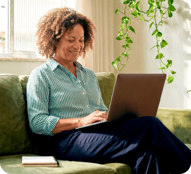 Mulher madura sorrindo em casa sentada no sofá usando o notebook