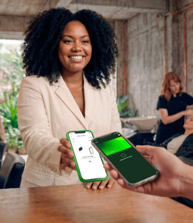 Empreendedora sorridente entregando o celular com TapStone aberto para cliente pagar por aproximação com o celular
