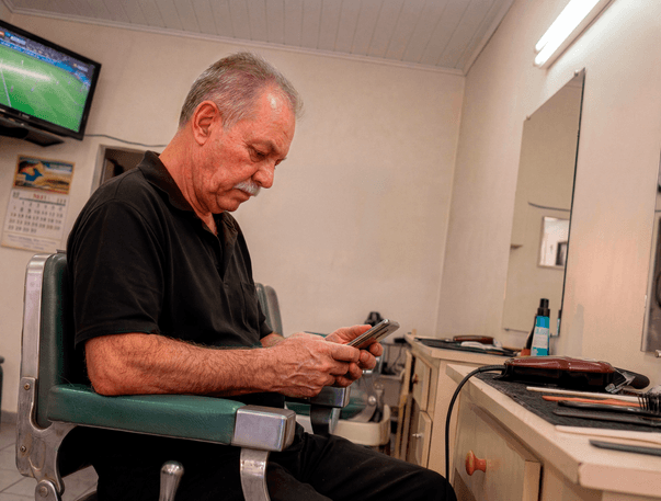 Senhor sentado em cadeira de barbearia consultando o celular