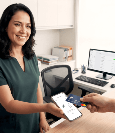 Profissional de saúde sorridente em consultório recebendo pagamento por aproximação no celular com cartão Mastercard