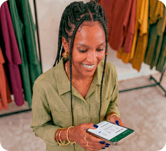 Empreendedora em loja de roupas sorrindo enquanto consulta o app Stone no celular