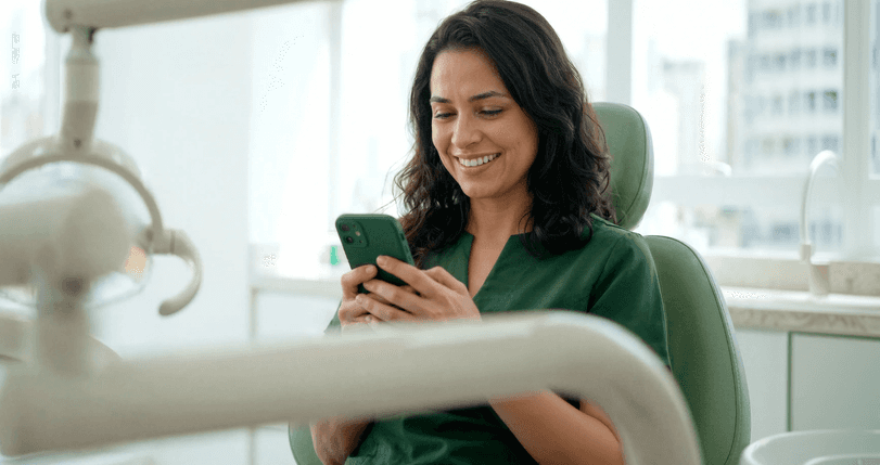 Dentista sorridente em consultório odontológico consultando o celular