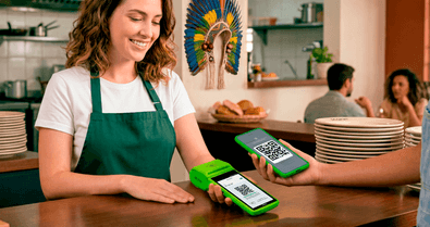 Atendente em restaurante segurando a maquininha Stone para cliente pagar via QR Code Pix com o celular