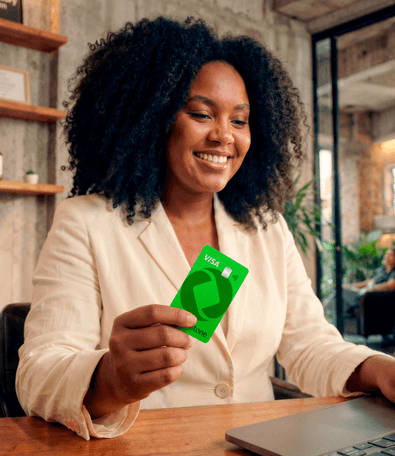 Empreendedora sorridente segurando o cartão verde Stone Visa enquanto usa o notebook