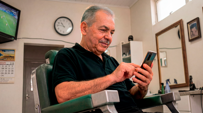 Senhor sentado em cadeira de barbearia consultando o celular