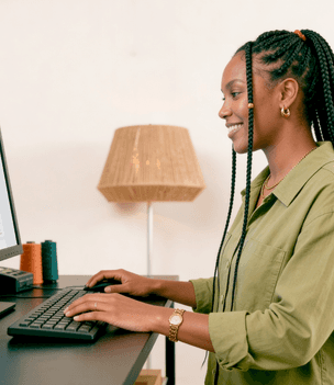 Empreendedora sorridente em ateliê de tricô digitando no teclado do computador