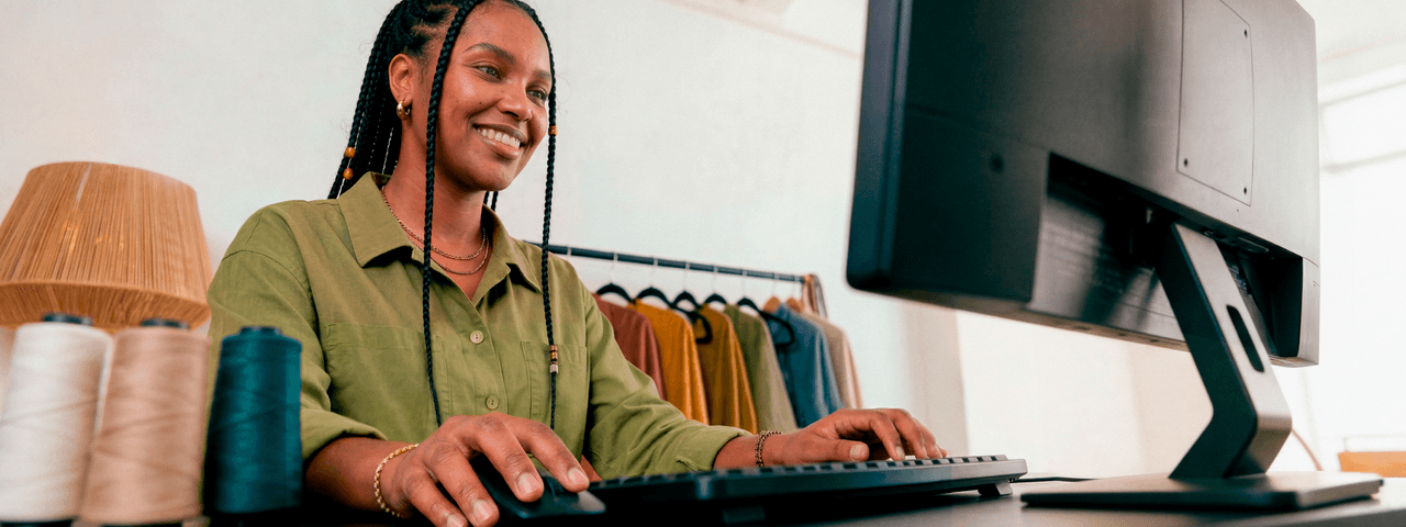 Empreendedora sorridente em ateliê de tricô digitando no teclado do computador
