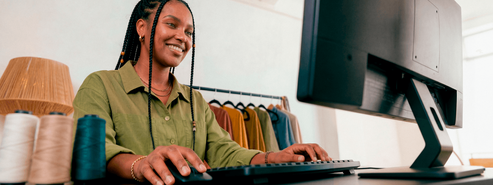 Empreendedora sorridente em ateliê de tricô digitando no teclado do computador