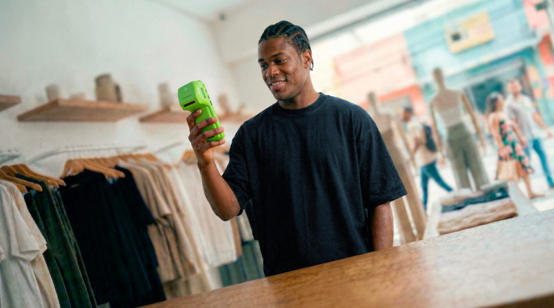 Empreendedor sorridente em loja de roupas masculinas exibindo a maquininha Stone