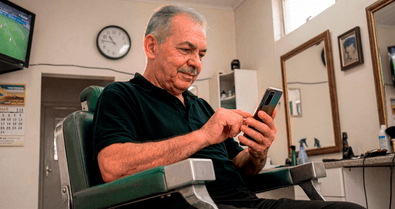 Senhor sentado em cadeira de barbearia consultando o celular