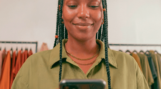 Empreendedora sorrindo em loja de roupas olhando para a tela do celular