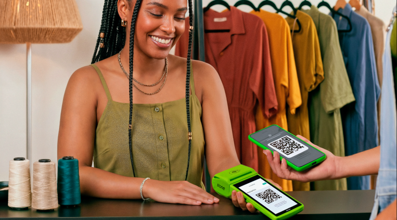 Empreendedora em loja de roupas recebendo pagamento via QR Code Pix na maquininha Stone