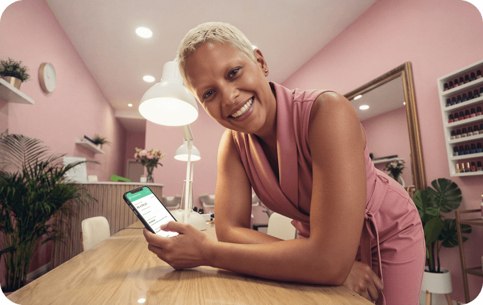 Empreendedora sorridente em salão consultando o app Stone no celular