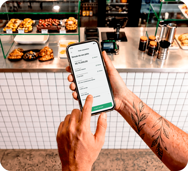 Mão segurando o celular com a tela de simulação de empréstimo Stone aberta, em padaria