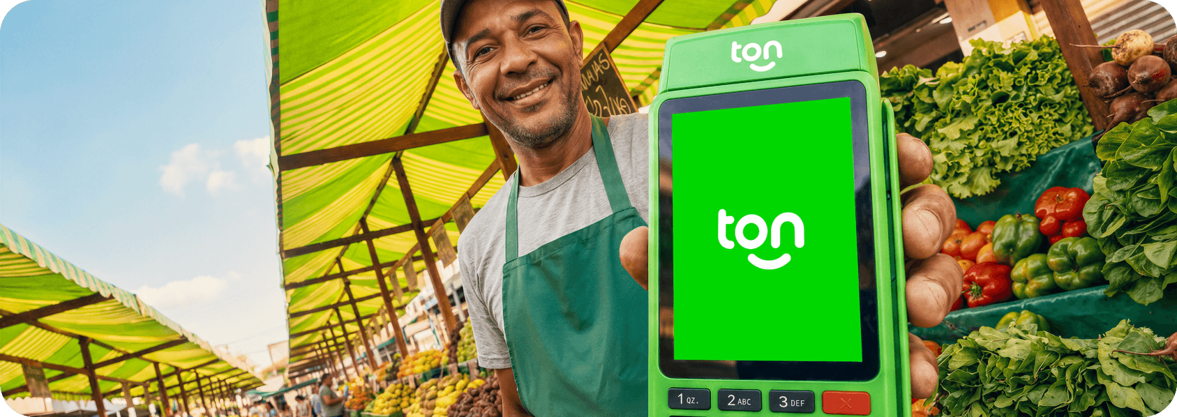 Empreendedor sorrindo segurando a maquininha Ton em sua banca de hortifruti