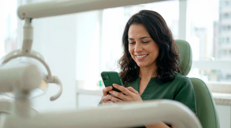 Dentista sorridente em consultório odontológico consultando o celular