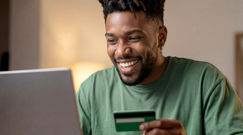 Empreendedor sorrindo em casa usando o notebook e segurando um cartão verde Stone