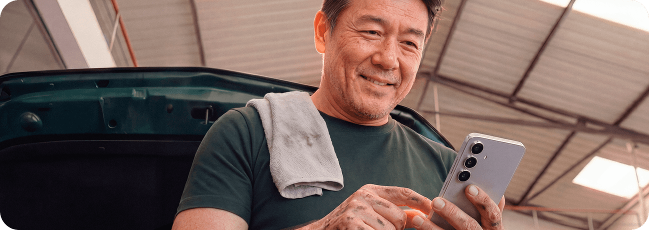 Empreendedor sorrindo segurando o celular em sua oficina mecânica