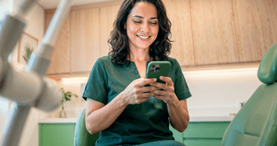 Dentista sorridente em consultório odontológico consultando o celular