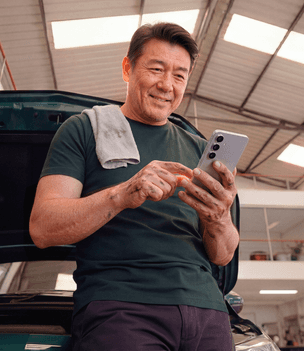 Mecânico em oficina sorrindo ao consultar o celular, com pano apoiado no ombro