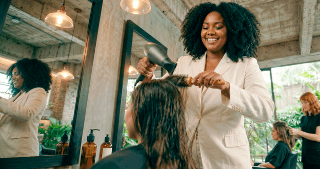 Cabeleireira sorridente escovando o cabelo de uma cliente em salão de beleza