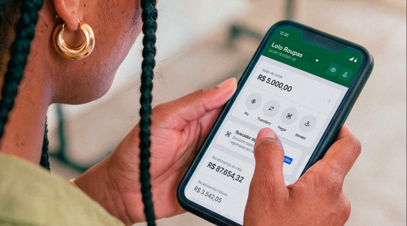 Mão segurando o celular com o app Stone aberto na tela de saldo da Lolo Roupas