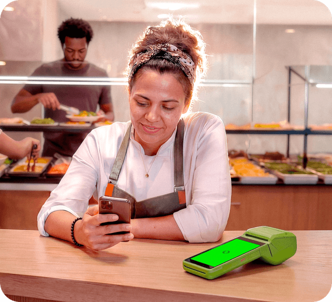 Empreendedora usando o celular ao lado da maquininha Stone em um restaurante