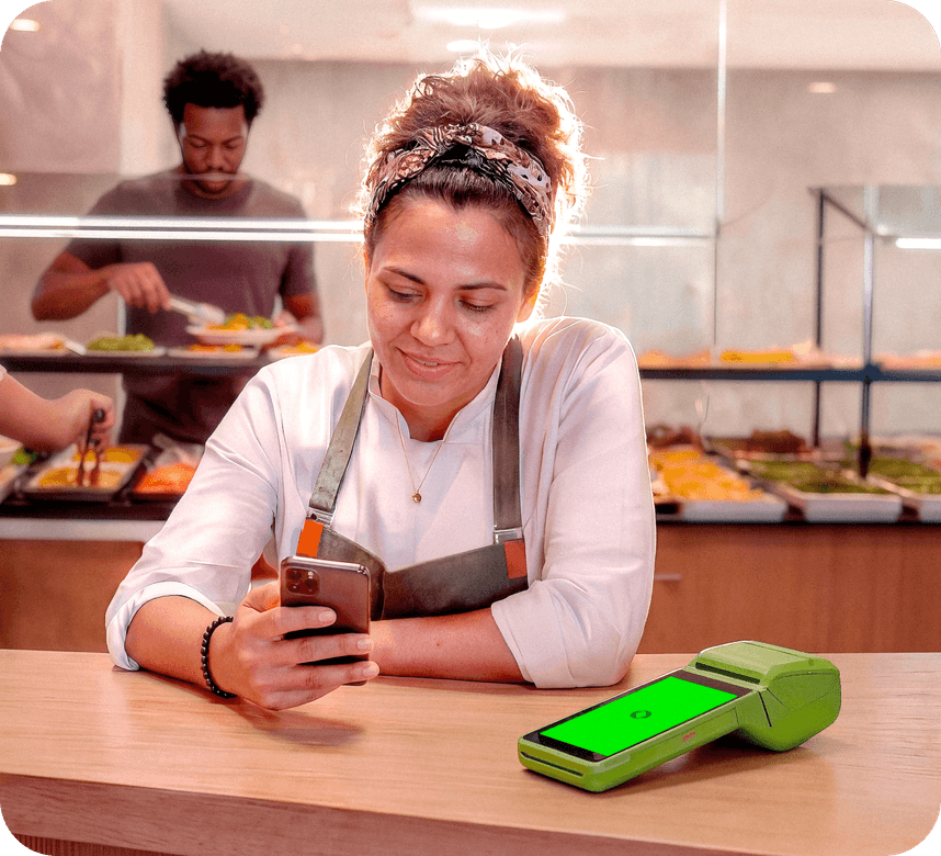 Empreendedora usando o celular ao lado da maquininha Stone em um restaurante