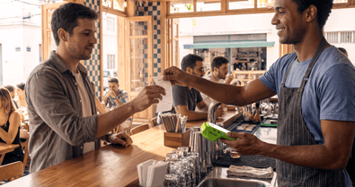 Atendente em balcão de bar entregando comprovante ao cliente, com a maquininha Stone na mão