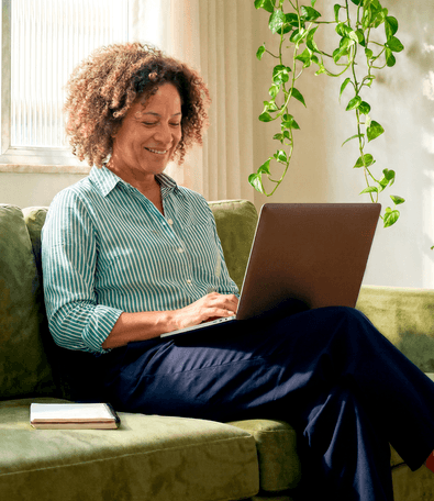 Mulher madura sorridente sentada no sofá de casa usando o notebook