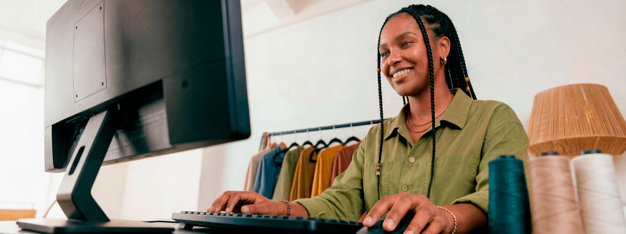 Empreendedora sorridente em ateliê de costura digitando no teclado do computador