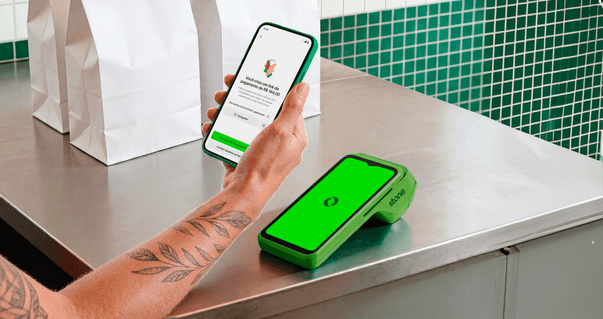 Sacolas de delivery em balcão ao lado de celular com app Stone e maquininha verde