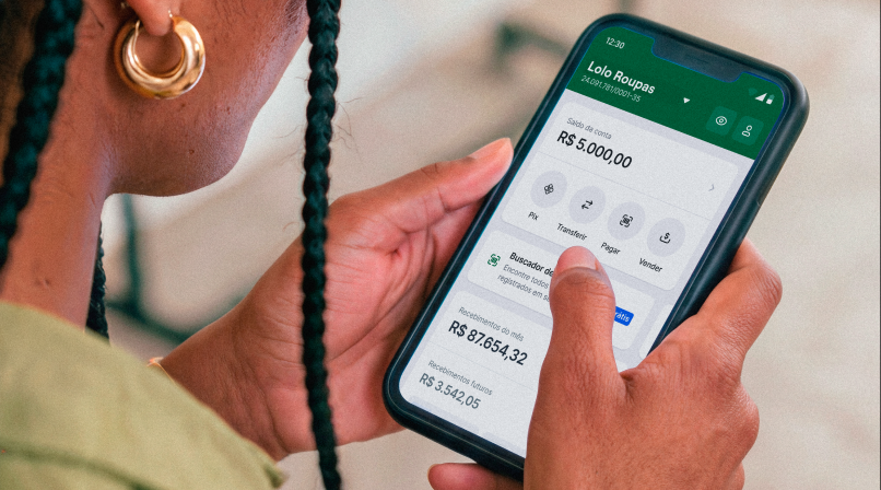 Mão segurando o celular com o app Stone aberto na tela de saldo da Lolo Roupas