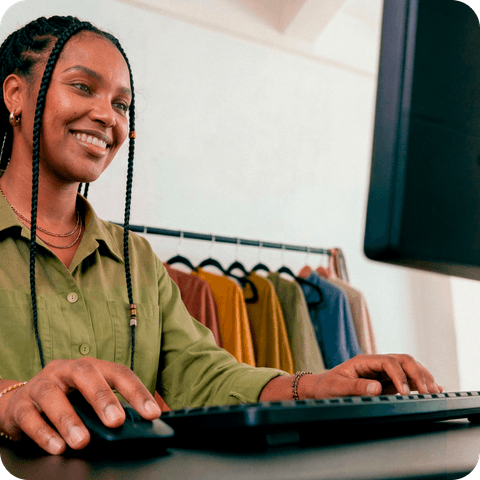 Empreendedora sorrindo enquanto trabalha no computador em sua loja de roupas