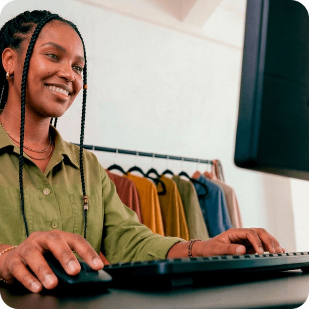 Empreendedora sorrindo enquanto trabalha no computador em sua loja de roupas