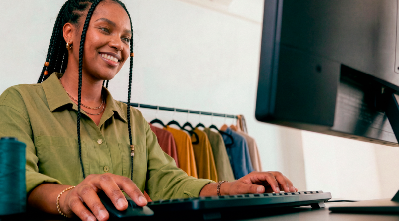 Empreendedora sorridente em loja de roupas digitando no teclado do computador