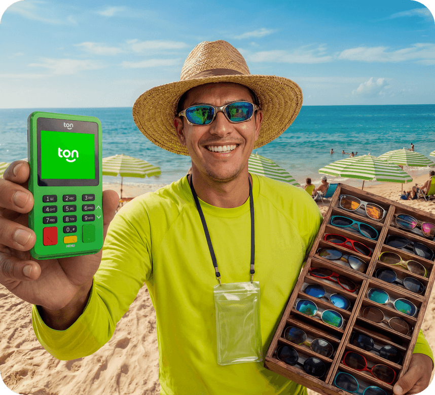 Vendedor ambulante sorrindo na praia mostrando a maquininha Ton