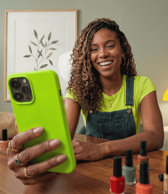 Mulher sorrindo e segurando o celular enquanto está sentada na mesa