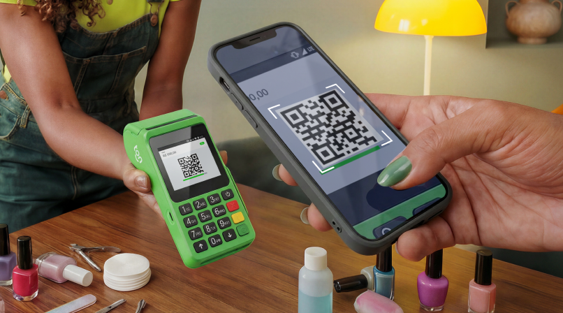 Mão segurando a maquininha Ton enquanto escaneia o QR Code de Pix