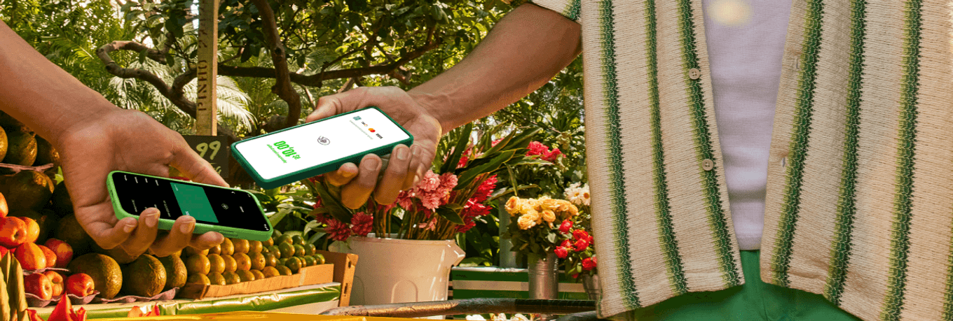 Empreendedor na sua barraca de laranja na feira com o seu celular recebendo o pagamento pelo Tapton, a maquininha no celular por aproximação do seu cliente.