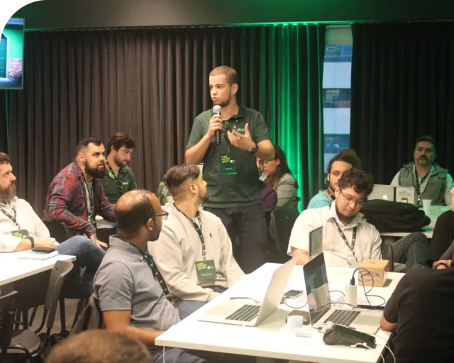 Rapaz da Stone de pé com microfone na mão fazendo uma fala para um escritório cheio