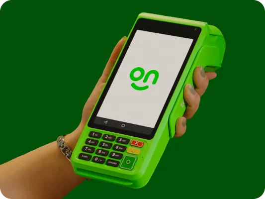 Mão segurando a maquininha do Ton em um fundo verde escuro