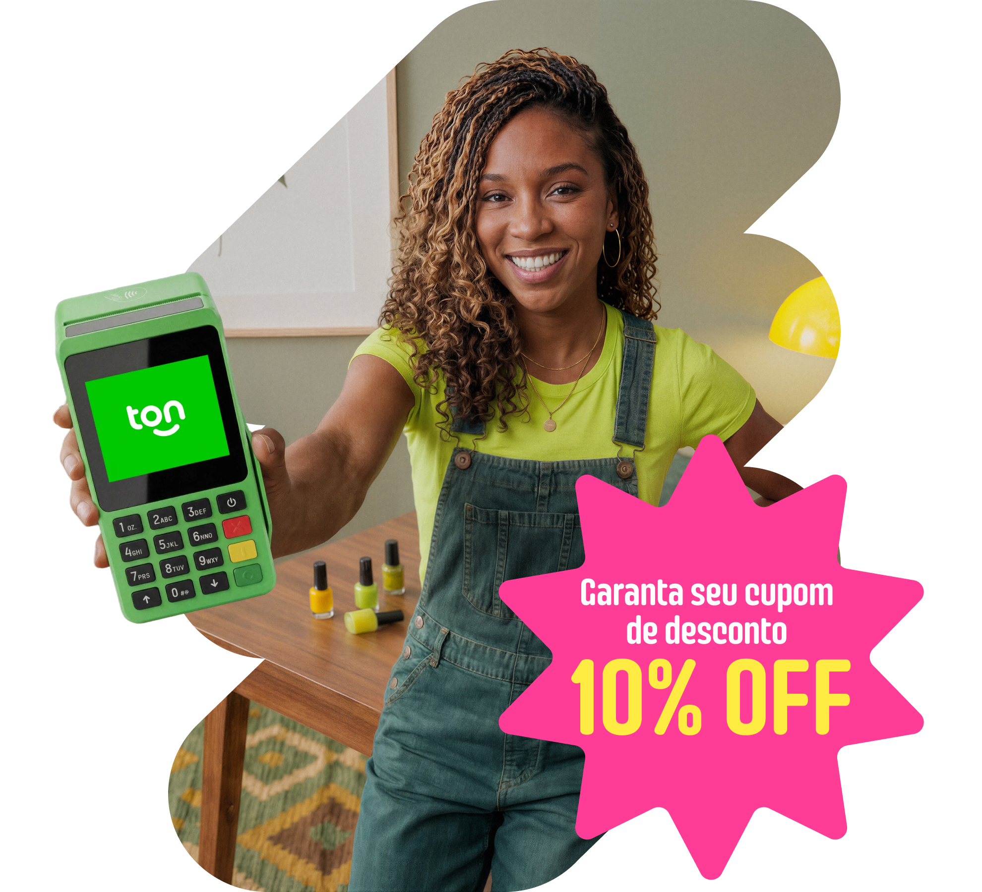 Empreendedora sorridente de macacão jeans estendendo uma maquininha Ton, com esmaltes sobre a mesa. Selo: 10% de desconto na maquininha.
