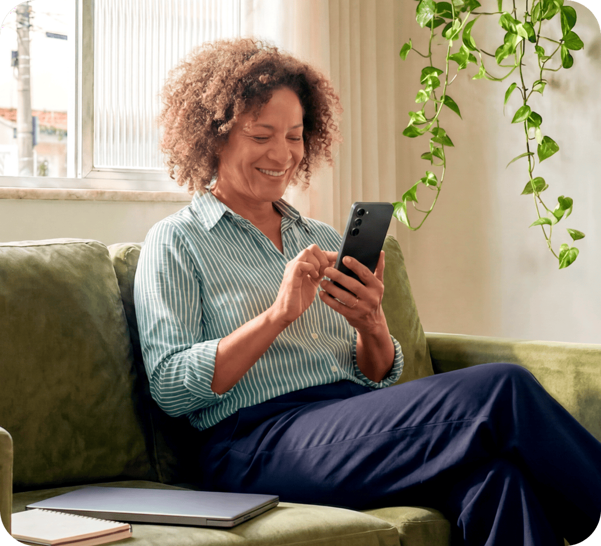 Empreendedora no sofá de casa sorrindo e observando a tela do celular nas mãos