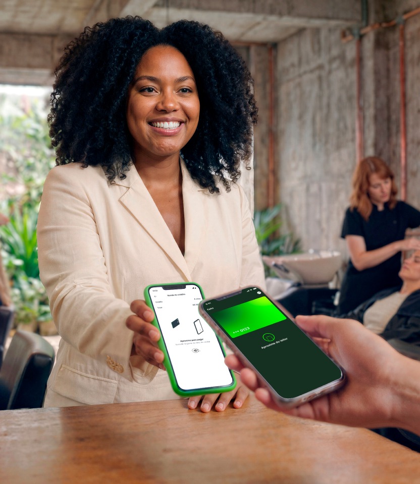 Empreendedora sorridente entregando o celular com TapStone aberto para cliente pagar por aproximação com o celular