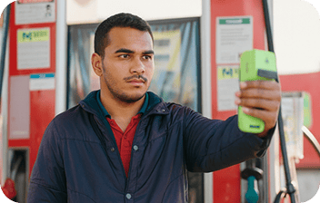 Homem em posto de gasolina segura a maquininha da Stone à altura do rosto para fazer reconhecimento facial ao bater o ponto.