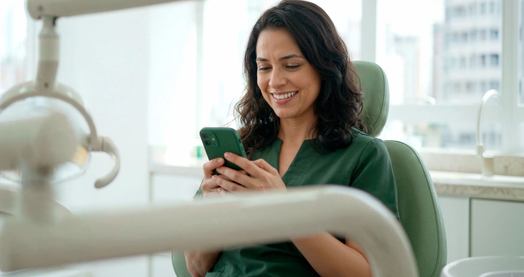 Dentista sorridente em consultório odontológico consultando o celular
