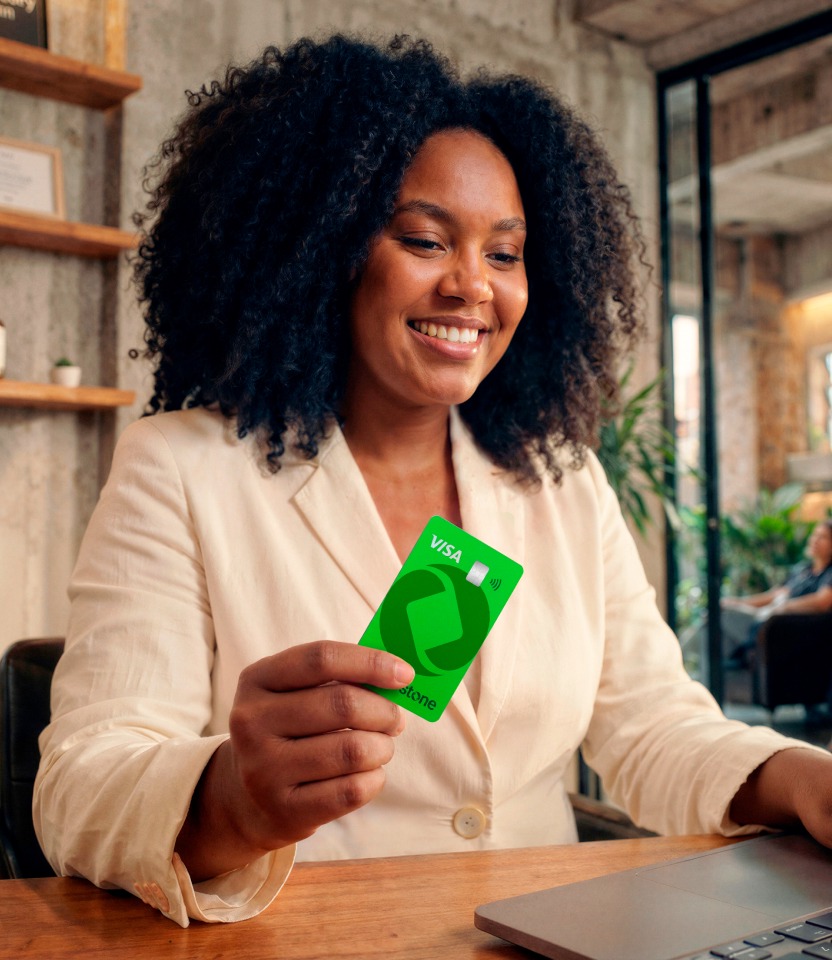 Empreendedora sorridente segurando o cartão verde Stone Visa enquanto usa o notebook